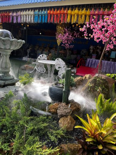 Jardín con fuente, plantas verdes y flores, decorado con cintas de colores.