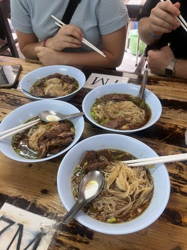 Cuatro cuencos de fideos con carne y cucharas, sobre una mesa de madera.