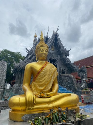 Buda dorado sentado frente a un templo con nubes grises en el cielo.