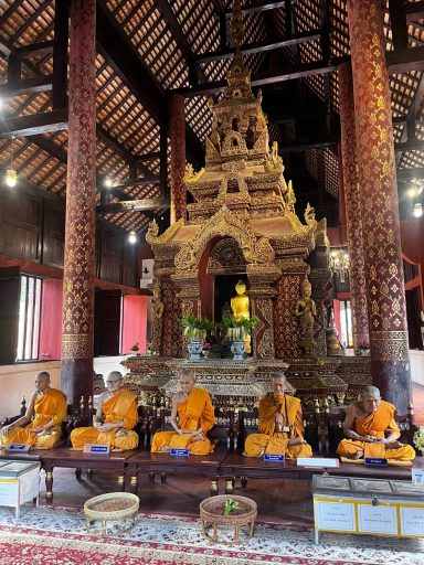 Estatua de Buda en un templo, rodeada por monjes budistas en meditación.