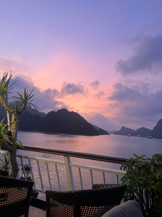 Atardecer sobre un lago rodeado de montañas, con vegetación en primer plano.