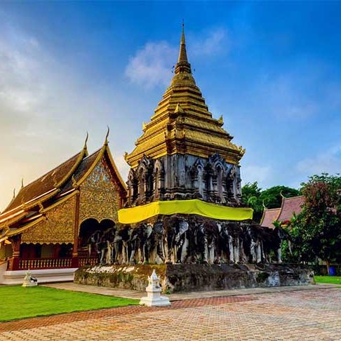 Stupa dorada con figuras en un templo rodeado de vegetación y cielo despejado.