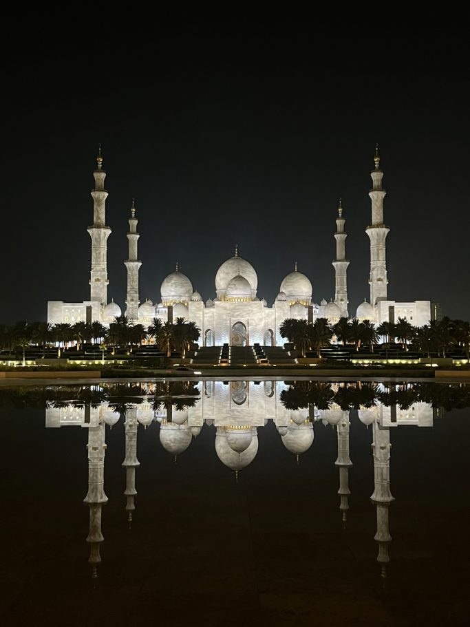 Gran mezquita iluminada por la noche, con reflejos en un lago tranquilo.