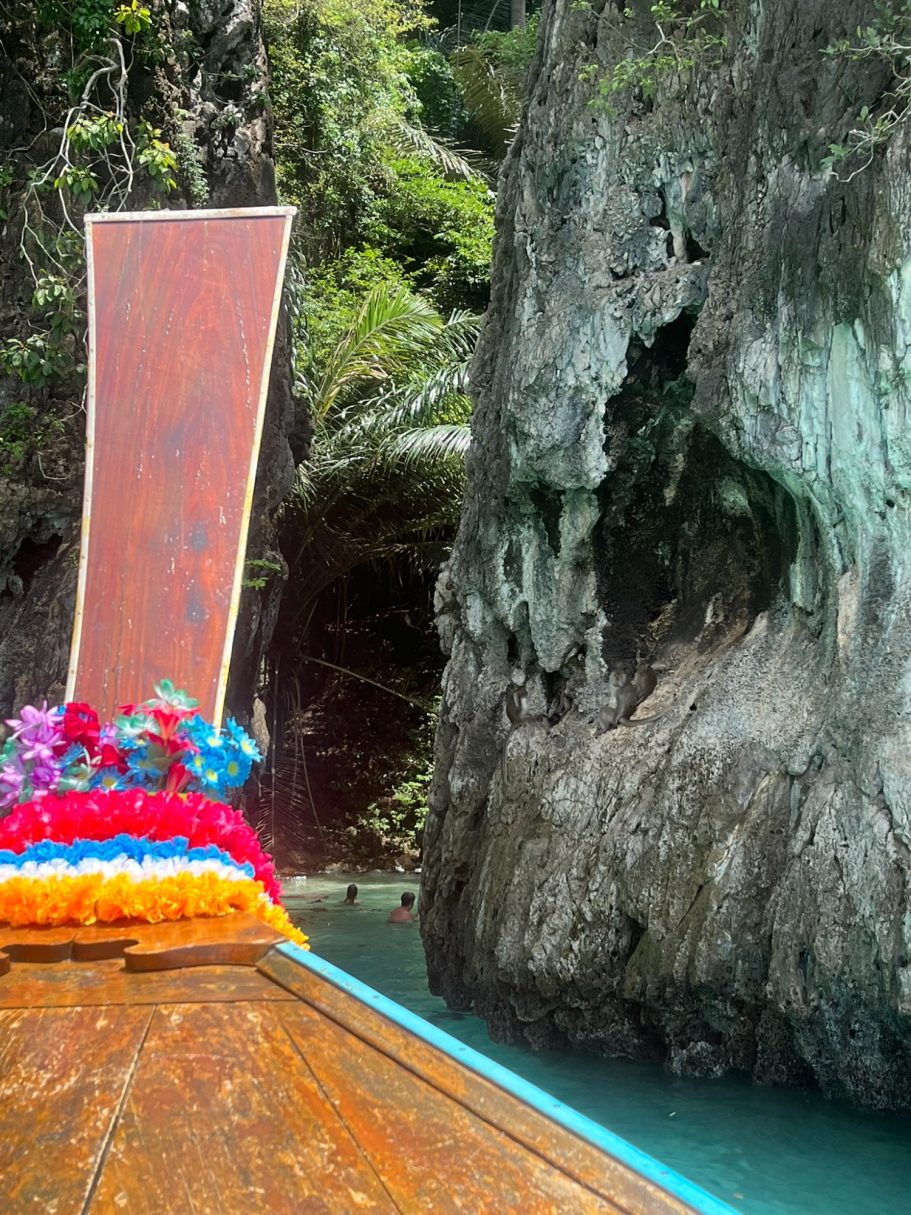 Proa de una embarcación colorida frente a un acantilado rocoso en un paisaje tropical.