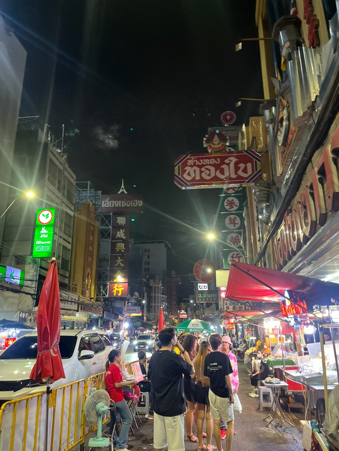Calle bulliciosa de noche, con luces brillantes y gente caminando entre los puestos.