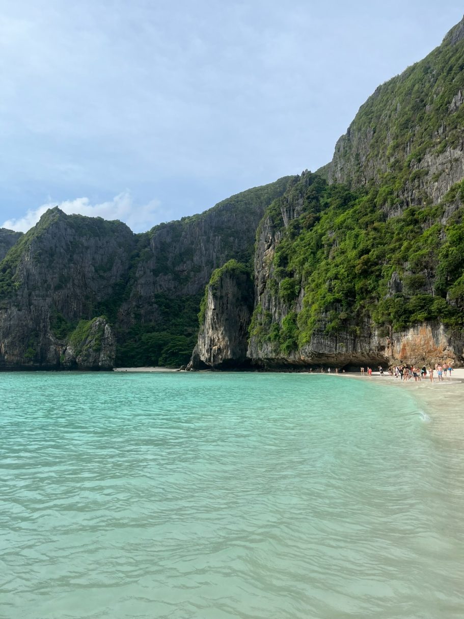 Playa con agua turquesa y acantilados verdes al fondo.