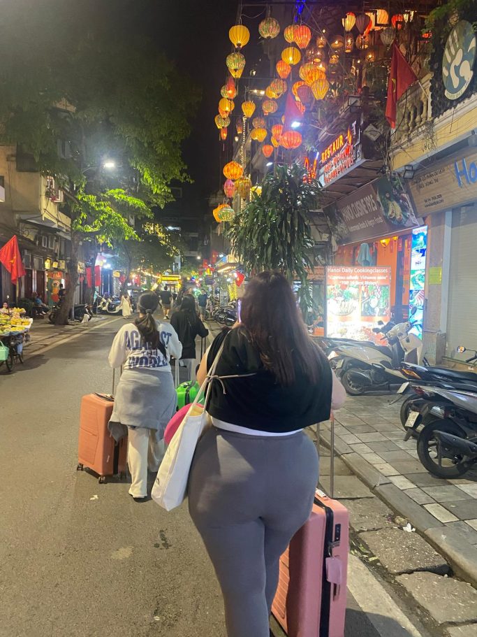 Personas caminando por una calle iluminada con faroles, llevando maletas.