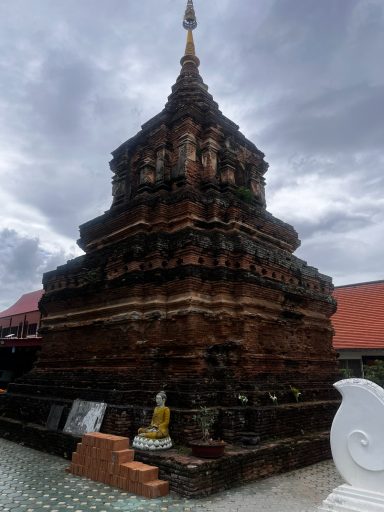 Estupa de ladrillo con un Buda en la base, rodeada de nubes grises.