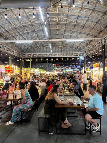 Mercado nocturno animado con muchas mesas y visitantes disfrutando de comida y bebida.