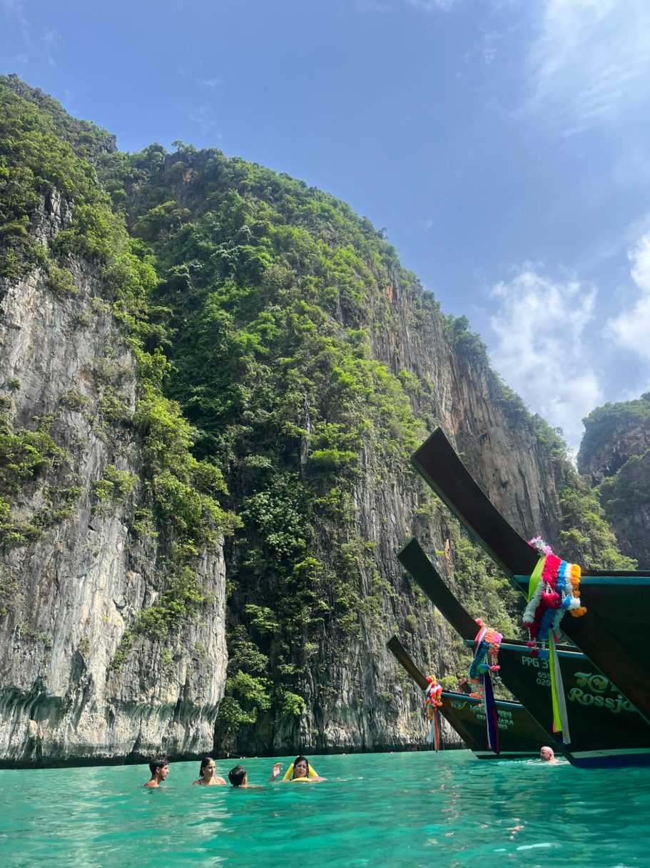 Grupo de personas en agua cristalina con acantilados verdes al fondo. Barco al lado.