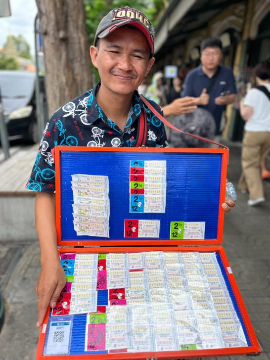Joven vendedor sonriente mostrando una colección de tarjetas en un estuche colorido.