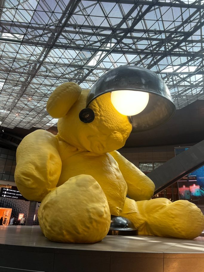 Oso de peluche amarillo con una lámpara en la cabeza, instalado en un espacio moderno.