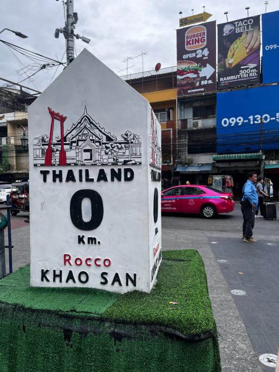 Señal kilométrica de Tailandia, marcador 0 km en Khao San Road. Fondo urbano.