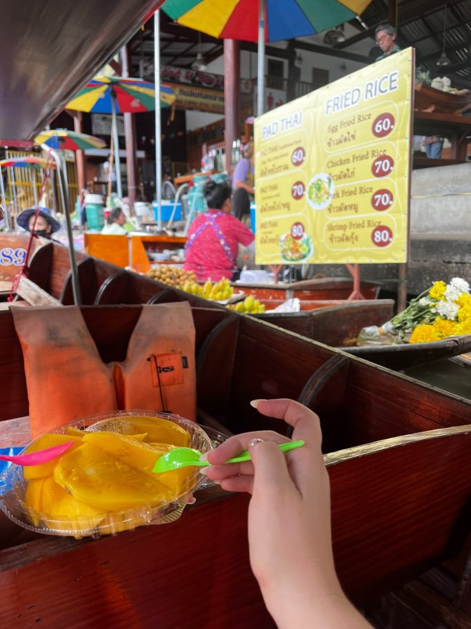 Mango fresco en un mercado, con sombrillas de colores y cartel de menú al fondo.