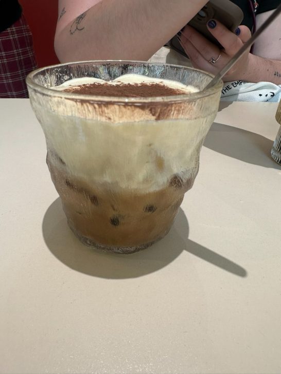 Vaso transparente con café, crema batida y cacao en polvo.