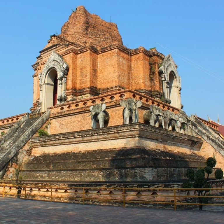 Templo antiguo con escaleras y estatuas, construido en ladrillo, bajo un cielo despejado.