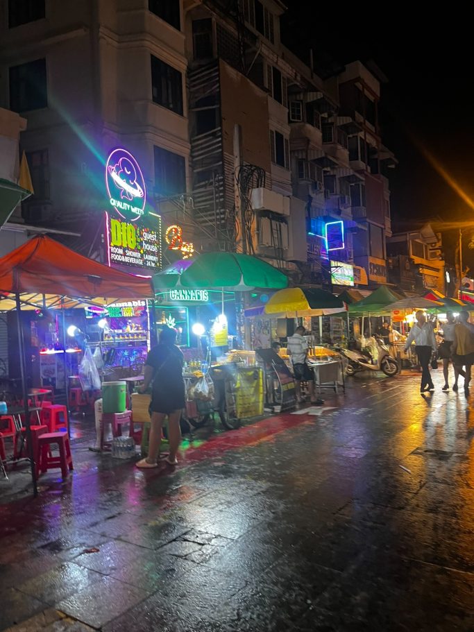 Puesto de comida callejera iluminado por neón en una noche lluviosa.