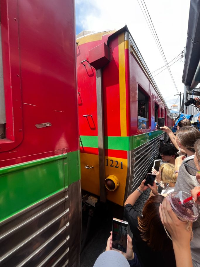 Tren de pasajeros pasa entre personas, en un área estrecha y concurrida.