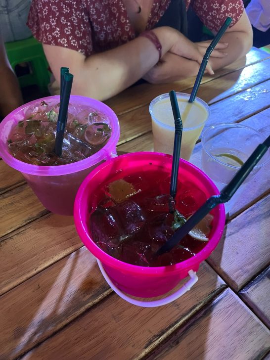 Dos recipientes de cócteles coloridos sobre una mesa de madera con pajillas.