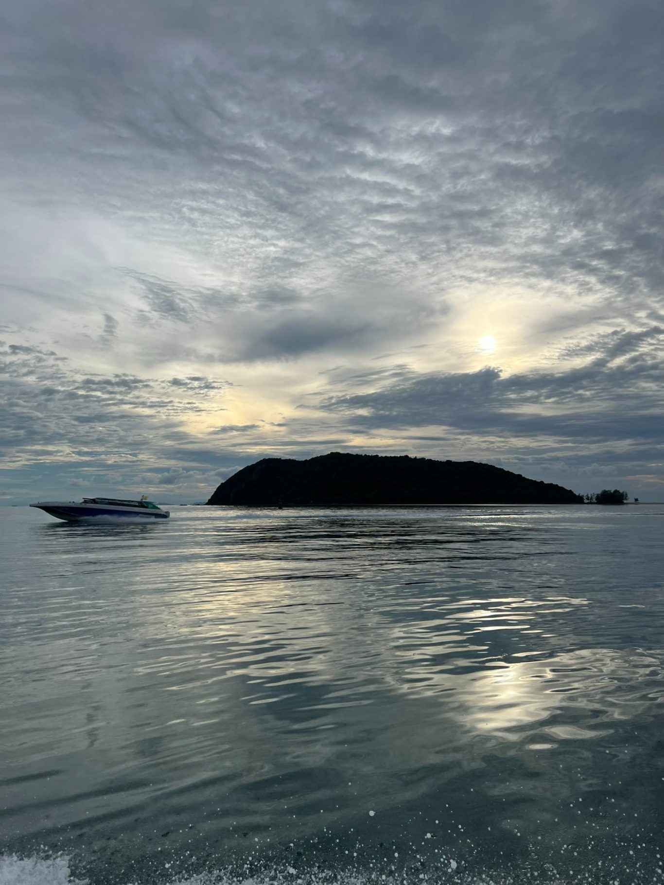 Paisaje marino al amanecer con una isla y un bote en el agua tranquila.