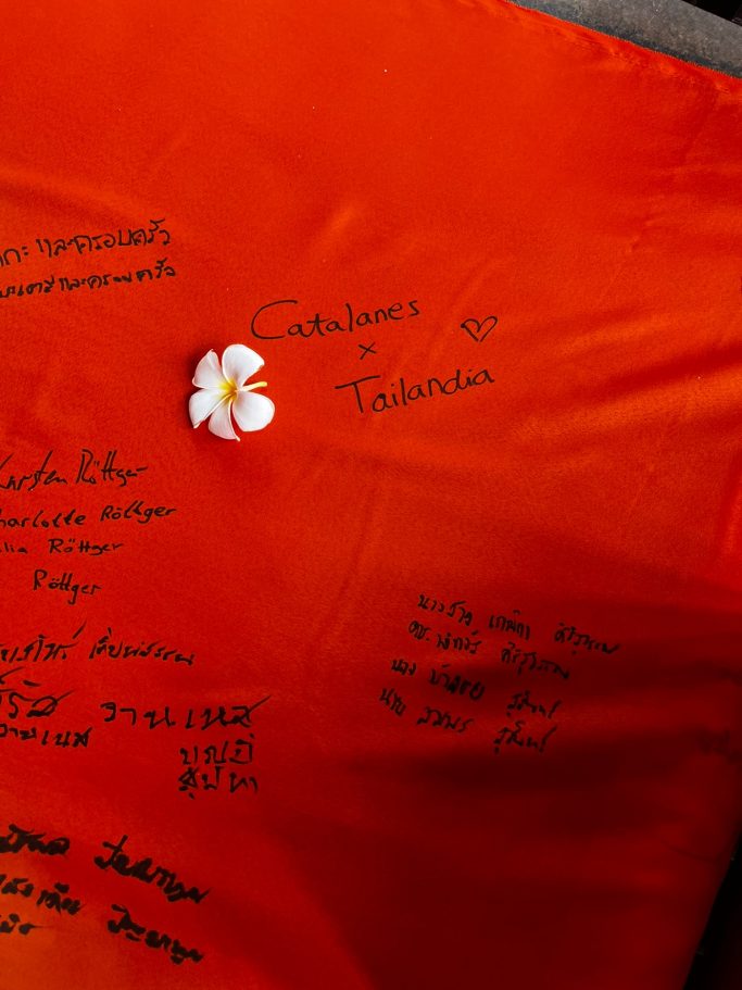 Tela roja con firmas y un flor blanca en la esquina.